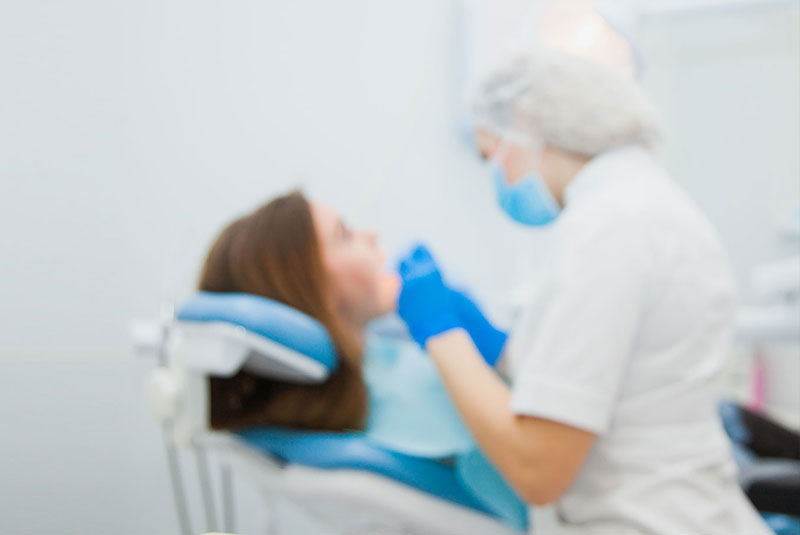Young female dentist curing patient's teeth filling cavity