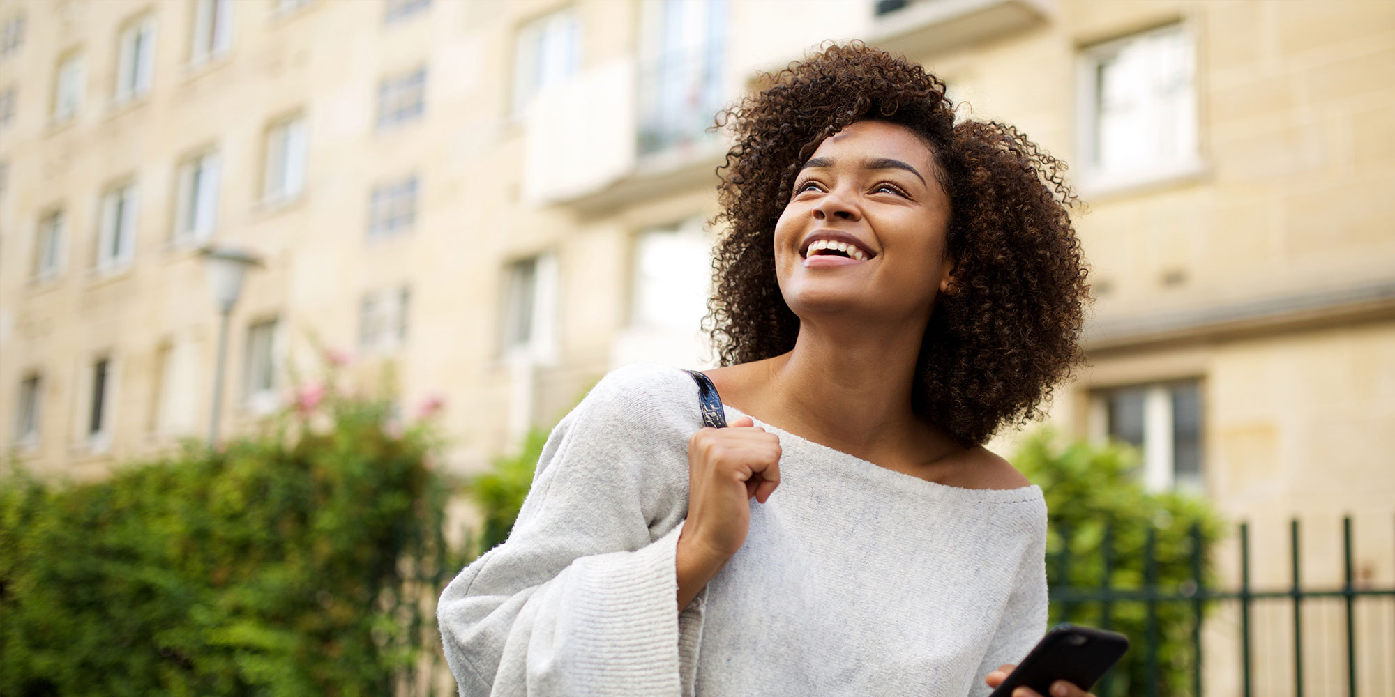 Portrait of smiling young african american woman walking in city with cellphone in hand